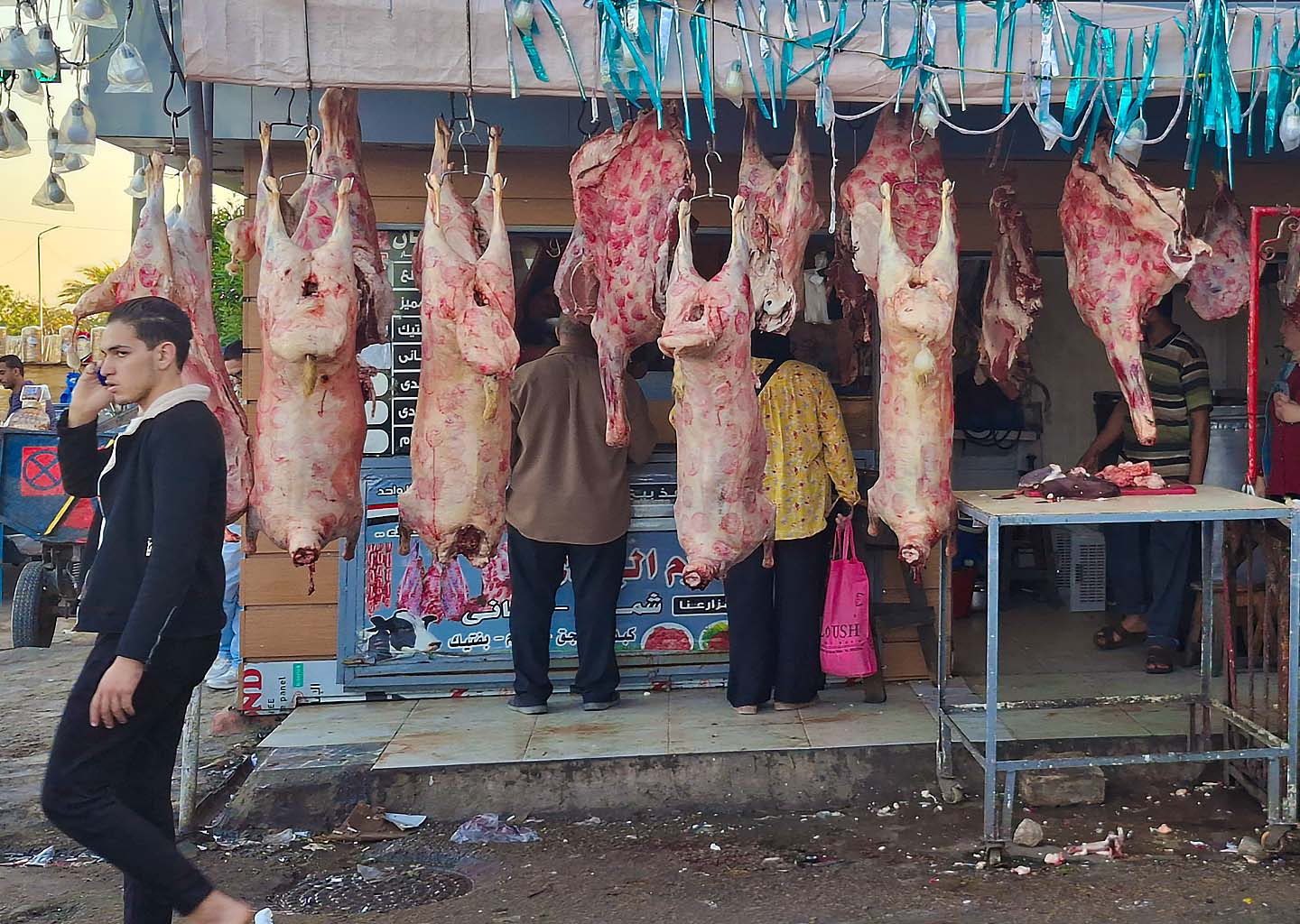 Puesto de carnicería callejera en Egipto con canales de carne colgadas y clientes comprando para la Fiesta del Sacrificio