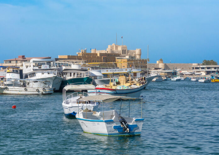 Barcos pesqueros y yates turísticos amarrados en el puerto de Alejandría, con la histórica Ciudadela de Qaitbay al fondo bajo un cielo despejado